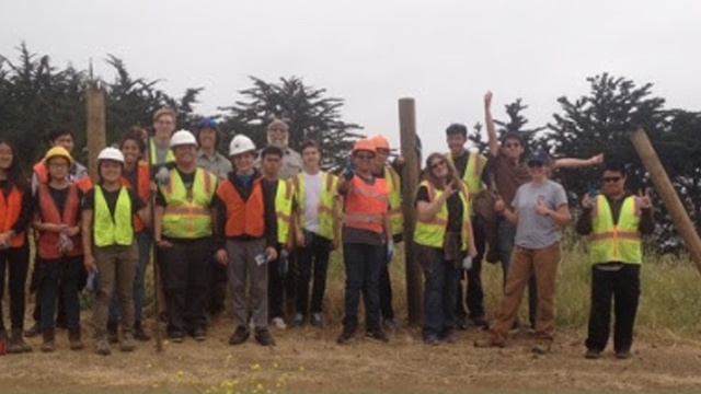A large group of people wearing bright colored safety gear pose outdoors
