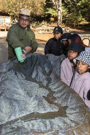 National Park ranger demonstrating waterflow into a model of Muir Woods to a group of young onlookers