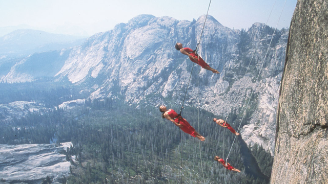 four people suspended from safety harnesses propel themselves away from the granite face of rock wall