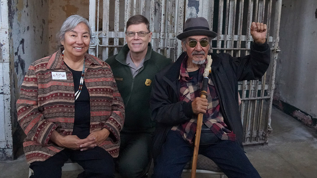 Three people sit smiling for the camera in the Alcatraz Cellhouse