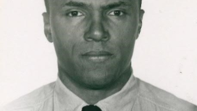 A black and white photograph of a Black man (Robert Lipscomb) in a white button-down shirt and a black tie. Presumably an intake photo for a federal prison.