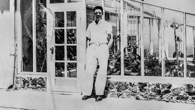 Historic black and white photo of Alcatraz inmate gardener Elliot Michener standing by the green house