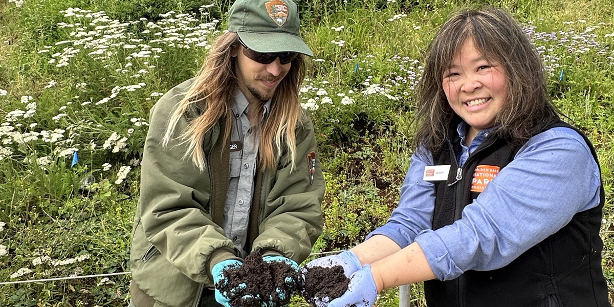 Two people hold up coffee grounds for a park project