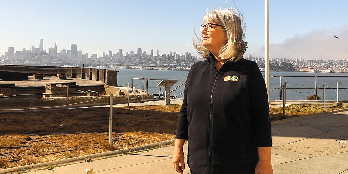 Nicki Phelps stands on Alcatraz Island with a view of San Francisco behind her.