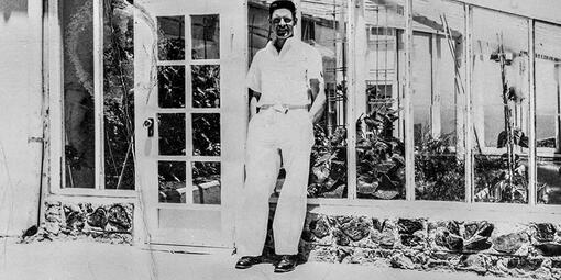 Historic black and white photo of Alcatraz inmate gardener Elliot Michener standing by the green house