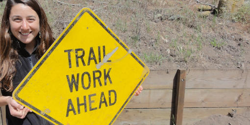 woman holding sign that says "Trail Work Ahead"