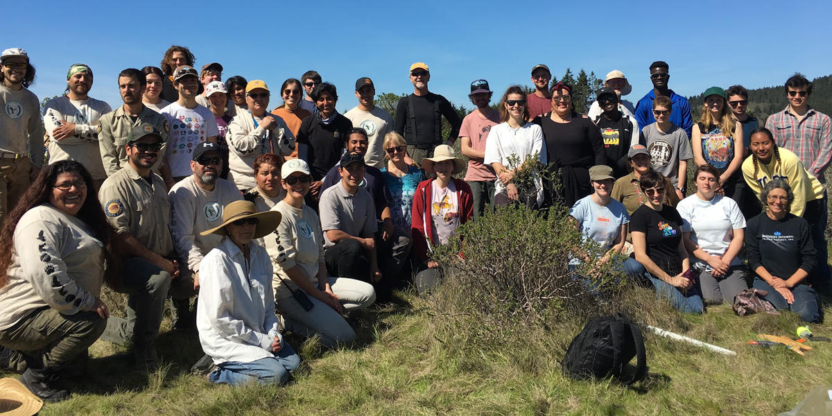 A large group of volunteers poses outside on a sunny day