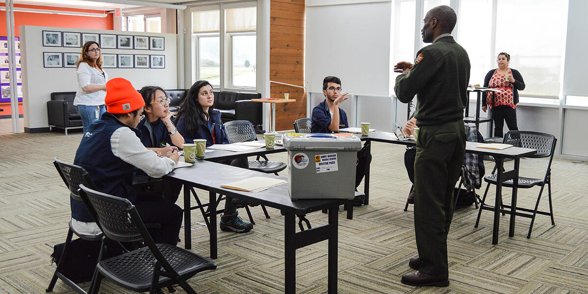 Educators in a classroom sit and listen to a National Park Service Ranger lecturing about educational techniques