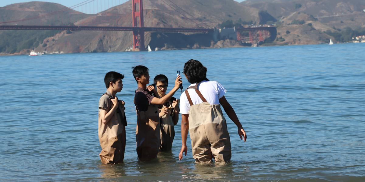 a small group of high school students learn to use environmental testing tools with an educator from the Crissy Field Center
