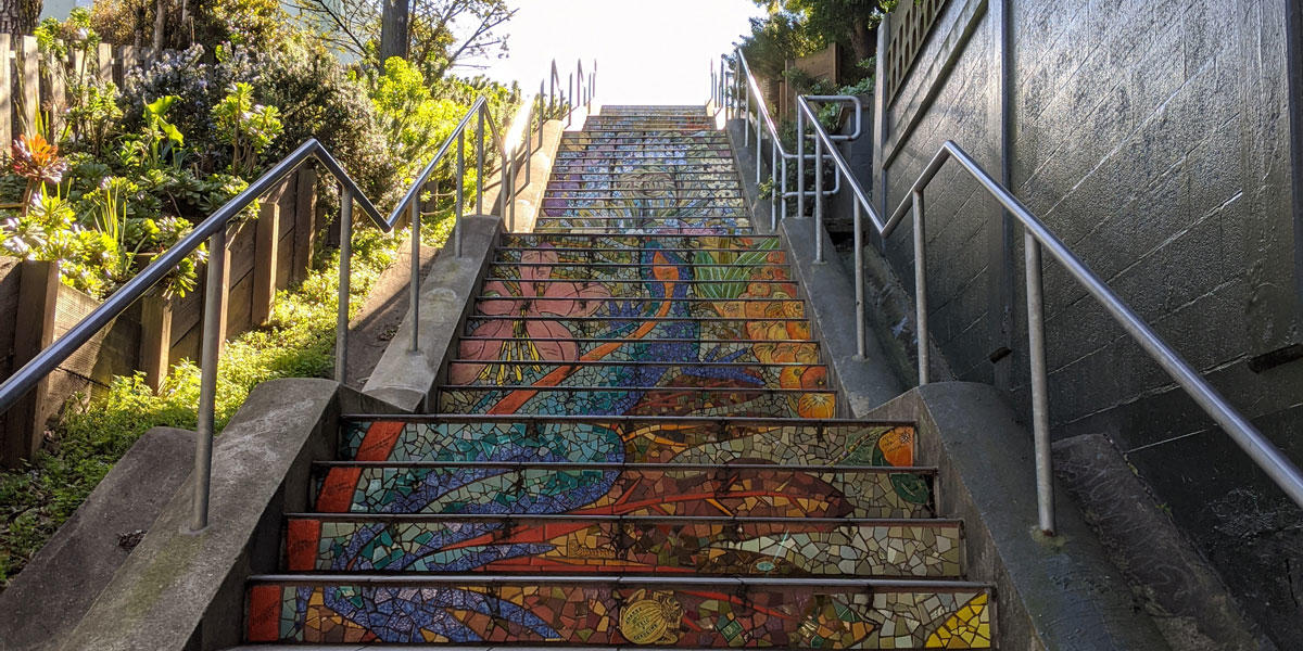 outdoor stairs adorned with colorful tiles are surrounded by plants and trees