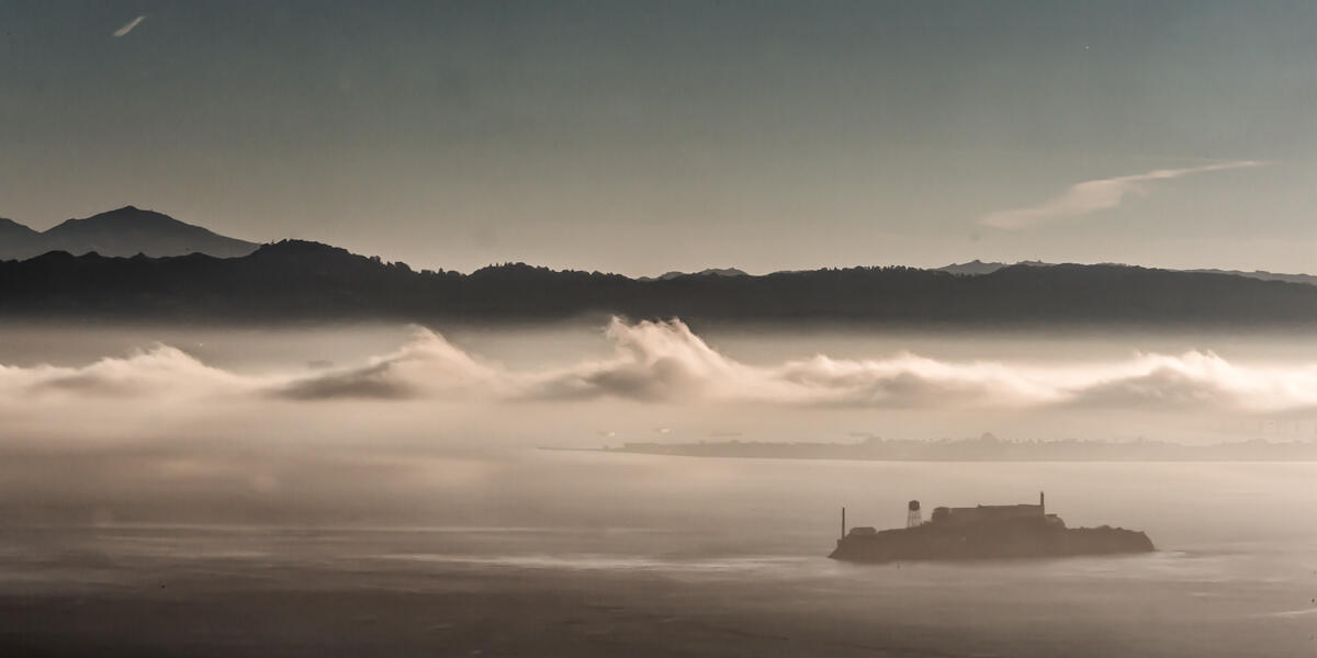 Alcatraz Island is pictured in the distance with dramatic gray clouds overhead.