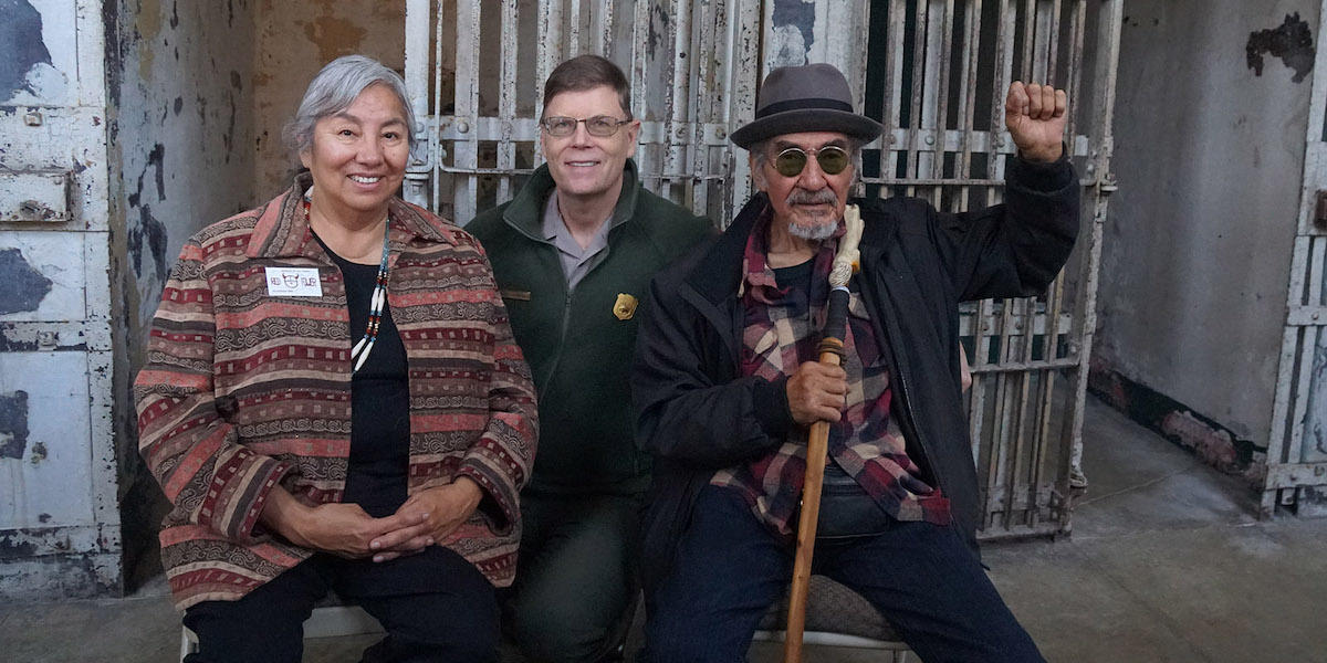 Three people sit smiling for the camera in the Alcatraz Cellhouse