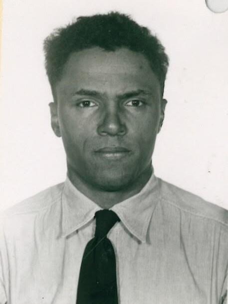 A black and white photograph of a Black man (Robert Lipscomb) in a white button-down shirt and a black tie. Presumably an intake photo for a federal prison.