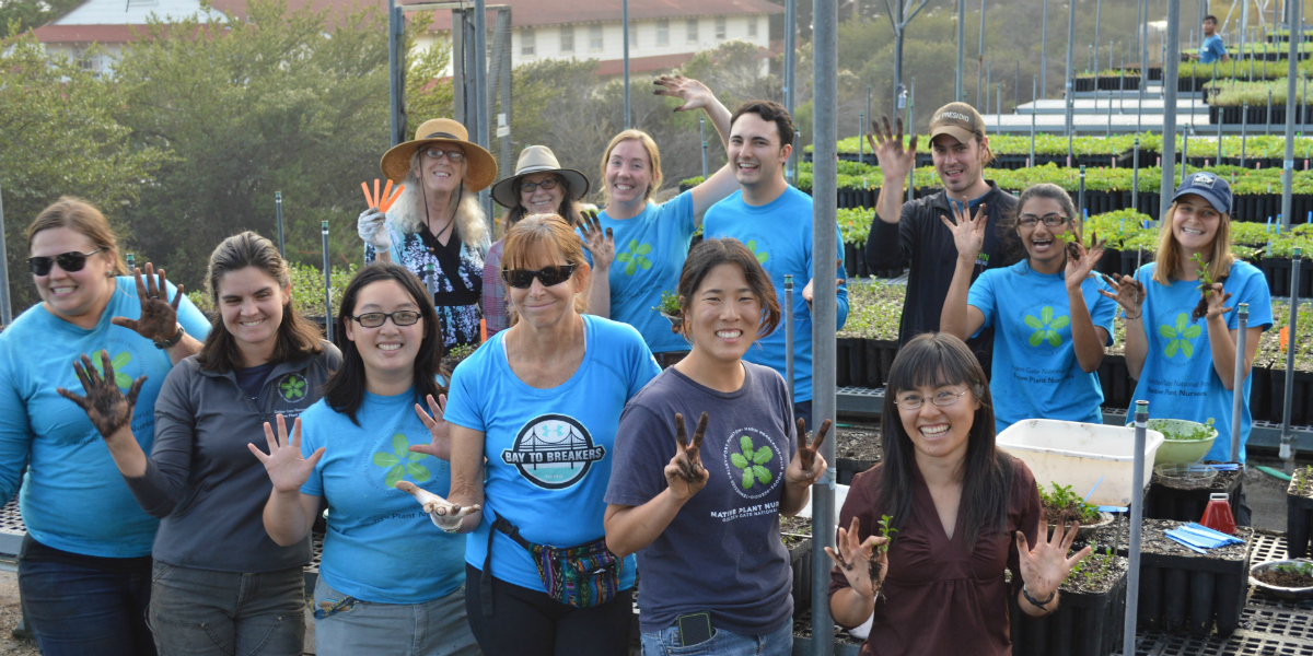 A large group smiles and holds up dirty hand while working in the nursery.