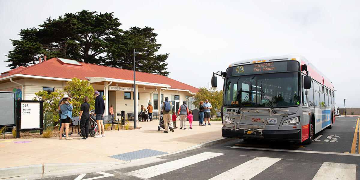 A red and gray San Francisco Muni bus parked at a station in the Presidio