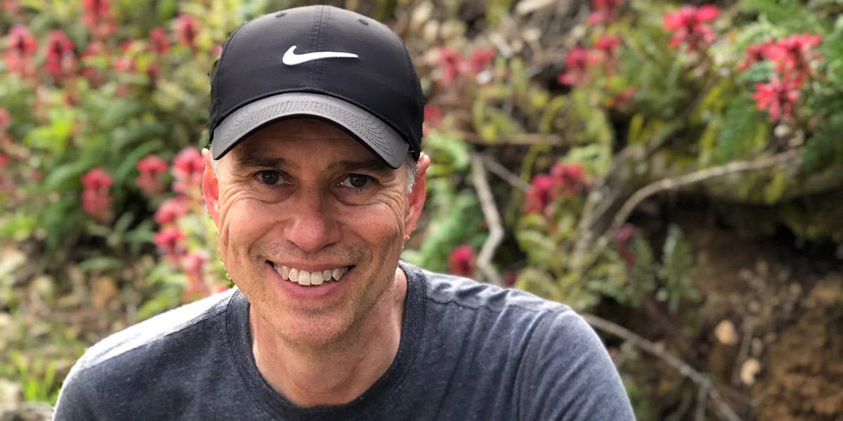 A volunteer smiles while seated in front of a blooming hedge