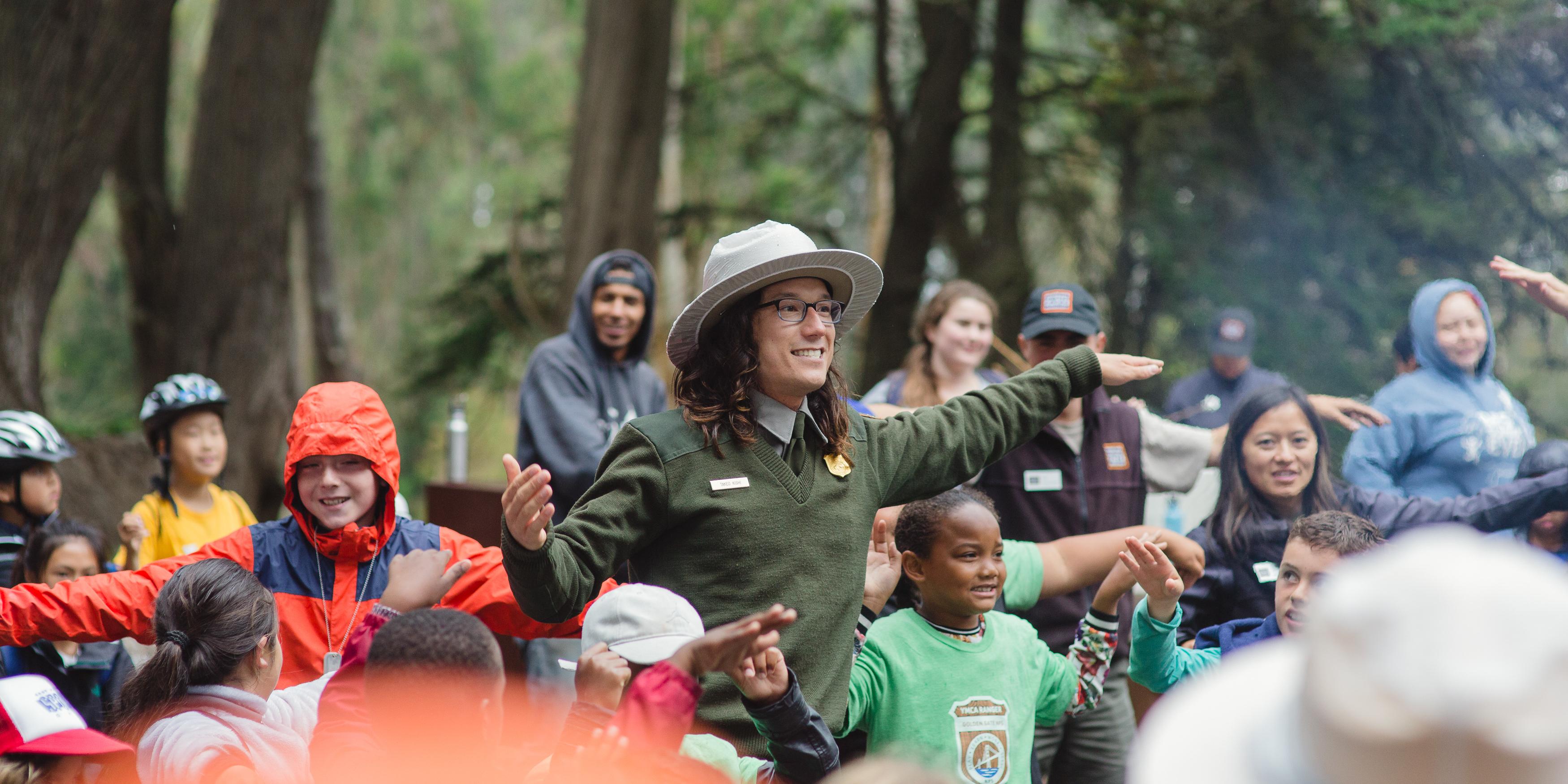 A National Park Service Ranger leads a large group of smiling children in an interactive story