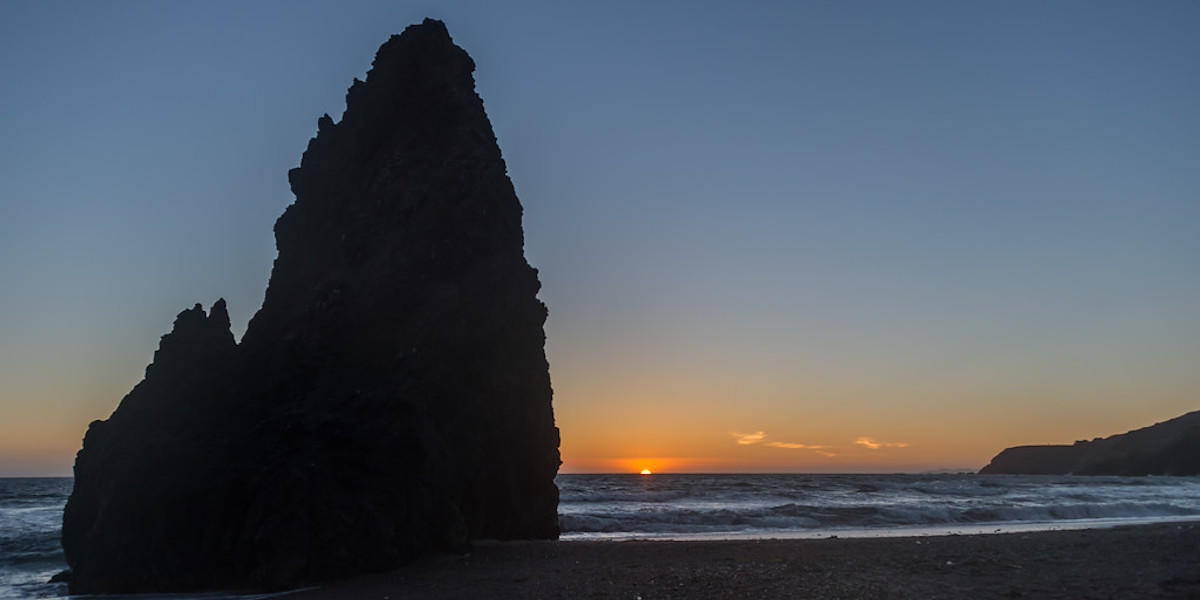 Sunset on the horizon with mitten-shaped rock formation on left.