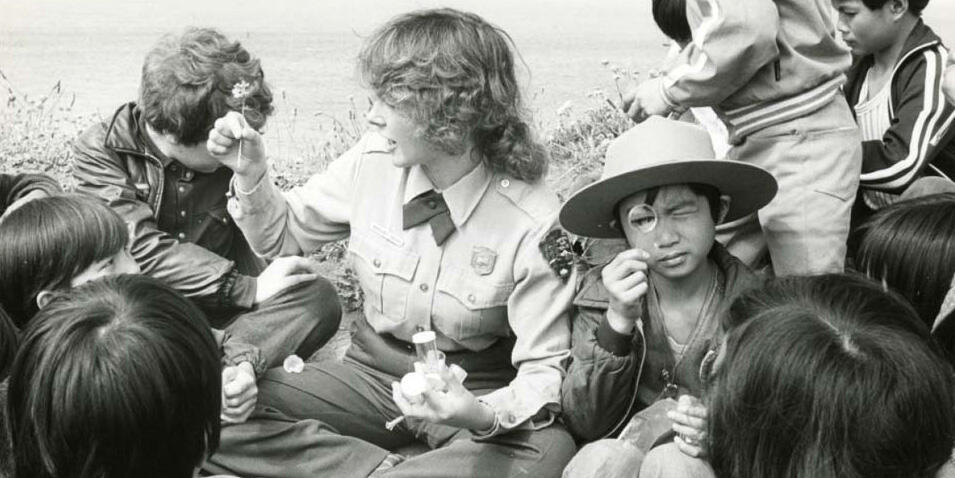 NPS park ranger, children gather and examine flowers in black and white historic photo from 1978.