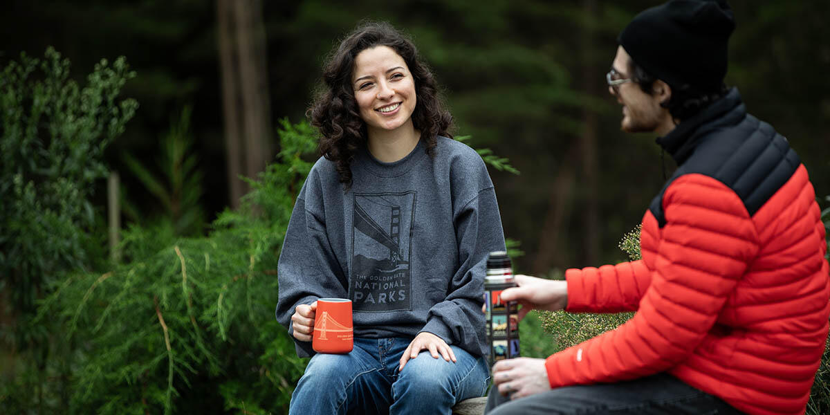Two people talk and hold mugs with parks in the background.