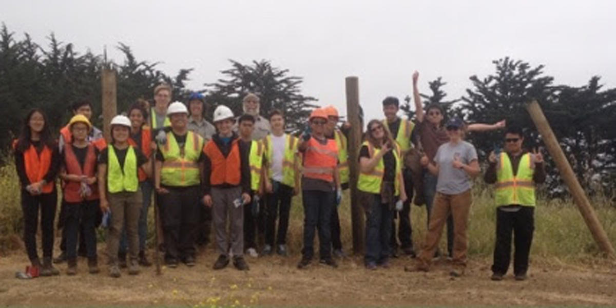 A large group of people wearing bright colored safety gear pose outdoors