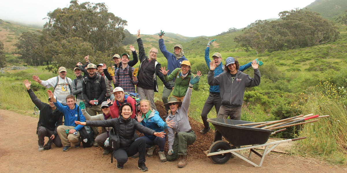 A group of volunteers joyfully pose after working outside on a trail