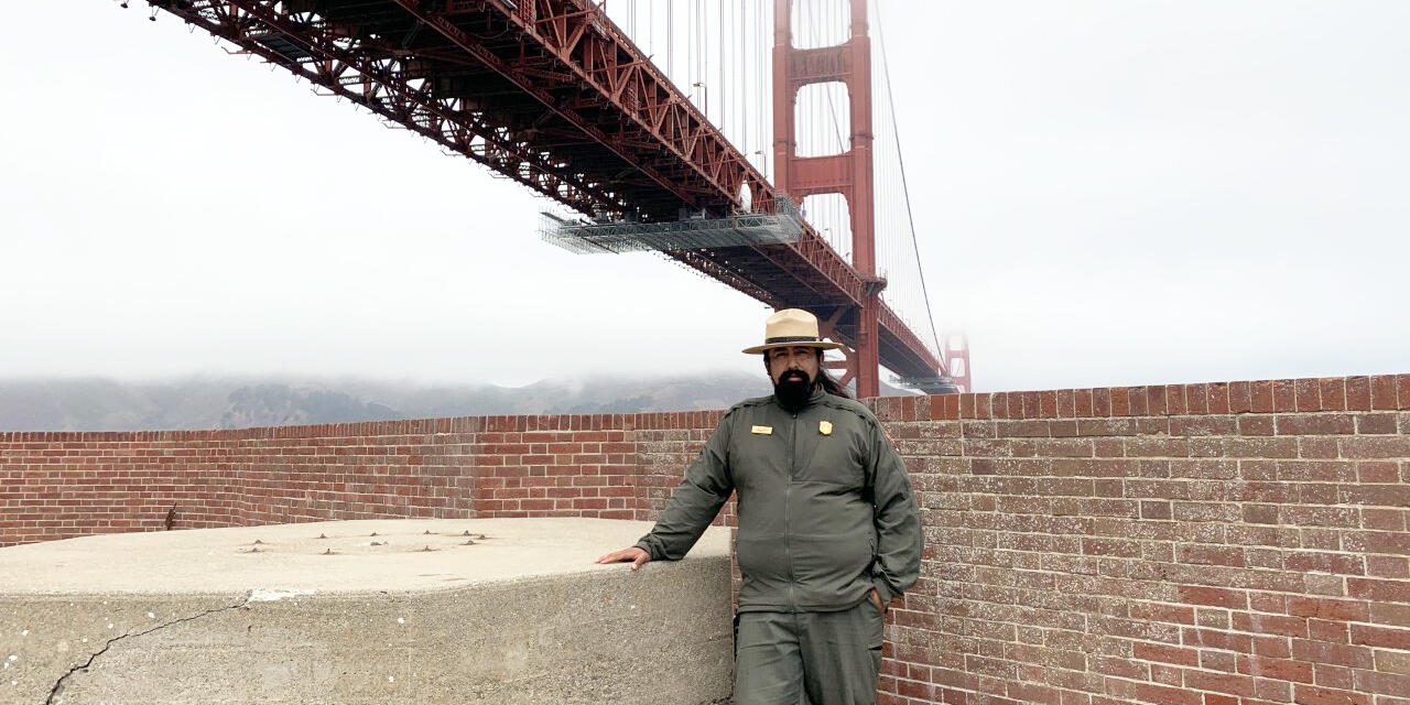 NPS Ranger Erick Cortes stands in front of the Golden Gate Bridge at Fort Point National Historic Site.
