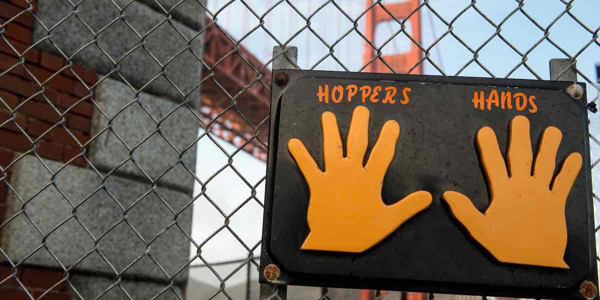 Sign labeled "Hopper's Hands" on a fence with the Golden Gate Bridge behind.