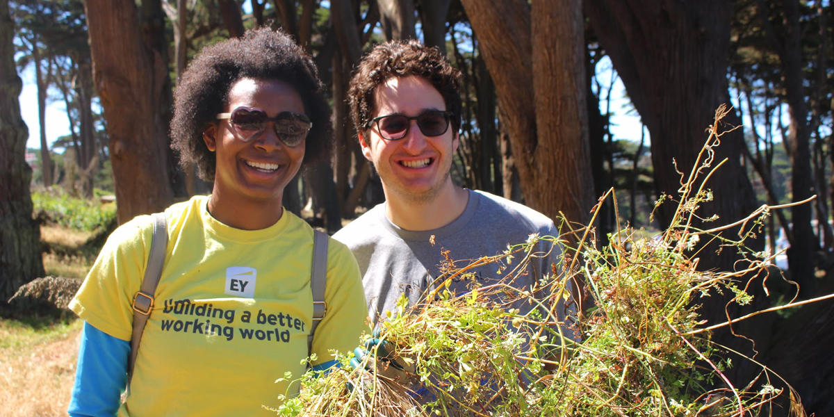 two people smile for the camera while holding plants they removed during a volunteer event