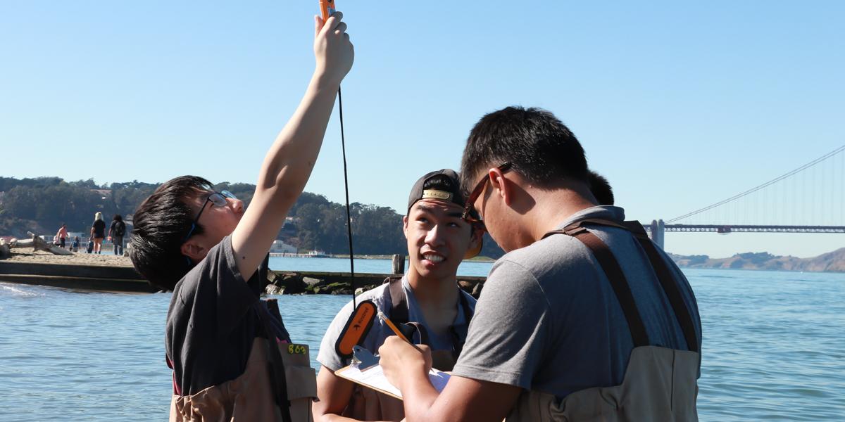 A small group of teenagers uses monitoring tools in the waters off of Crissy Beach