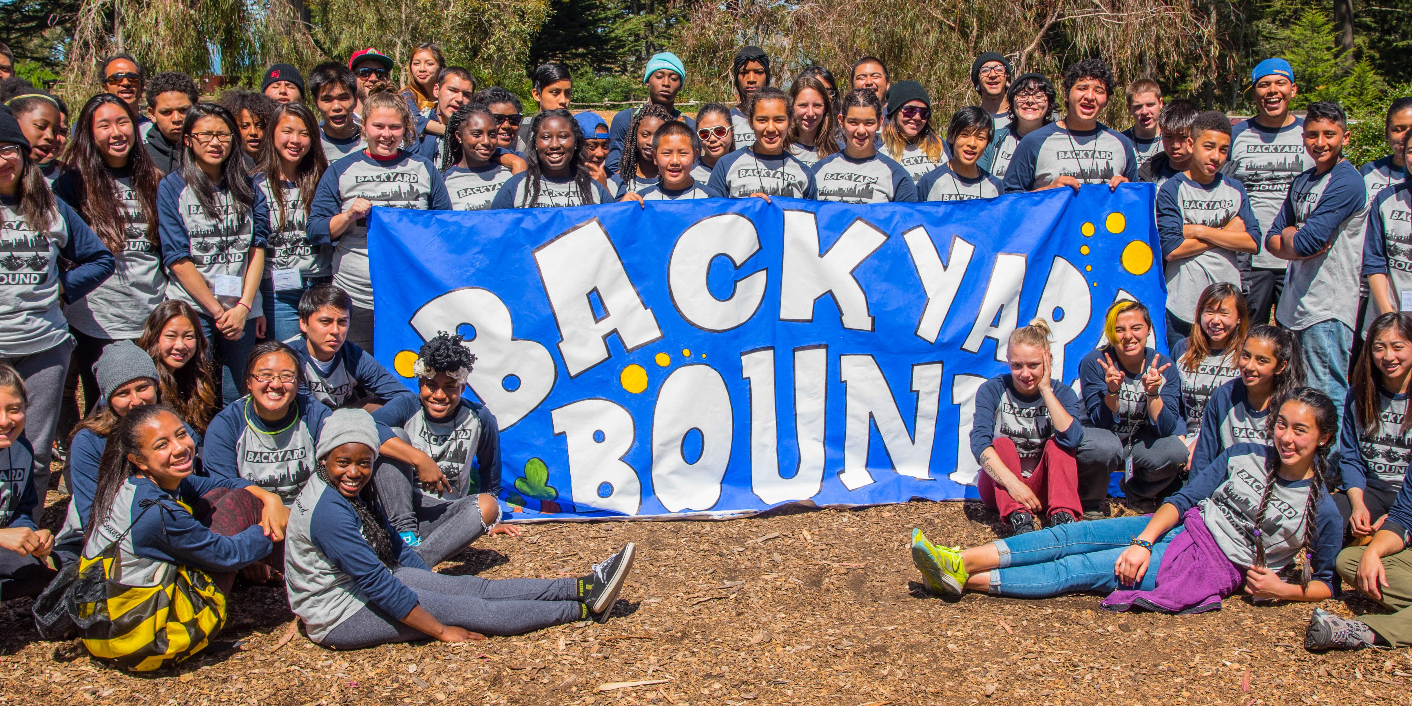 Backyard Bound Youth Summit Group Photo A large group of youth and youth workers gather around a banner reading Backyard Bound