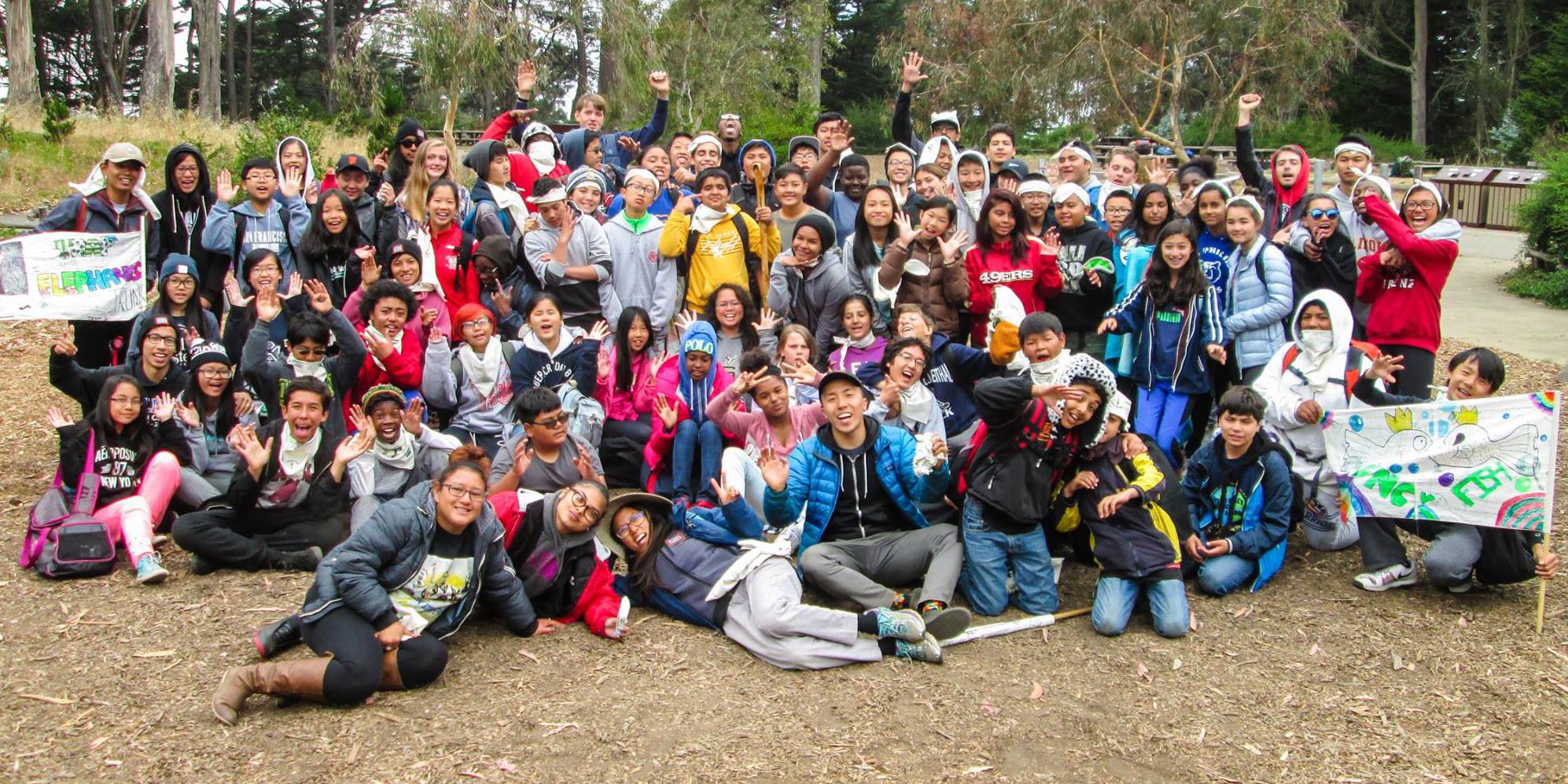 A large group of cheerful teenagers excitingly cheer at Rob Hill Campground in the Presidio of San Francisco