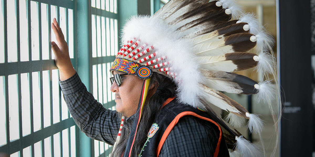 Man in native american headress looking out window of bars