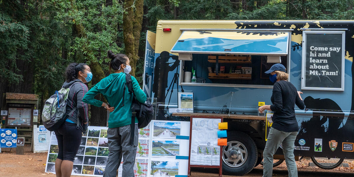 A masked staff member of ONE TAM greets park visitors with the Roving Ranger at Mount Tamalpais.