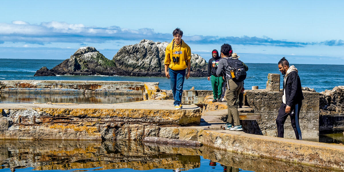 5 youth program participants walk amongst the sutro bath ruins at Lands End with an ocean backdrop on a sunny day