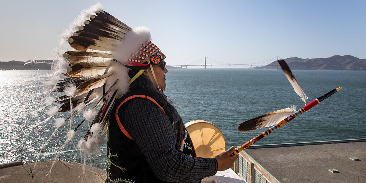 Profile of man with golden gate bridge in background.  The tide is going out and the sky is blue.