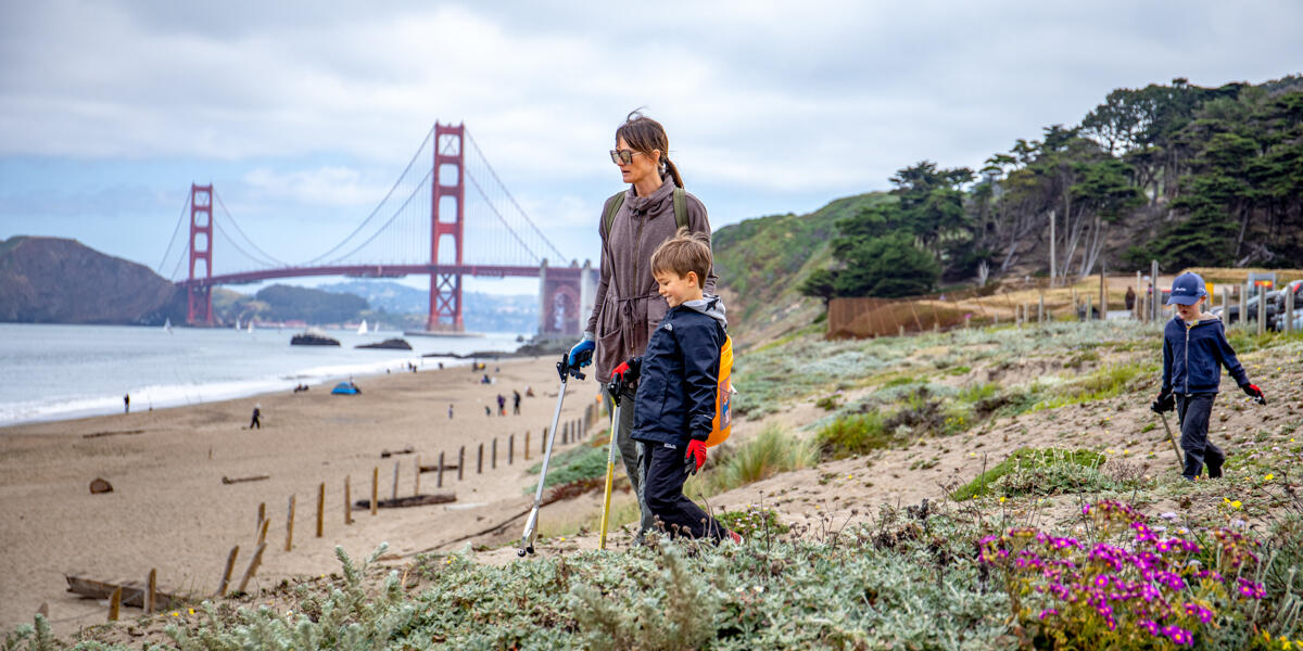 A family looks out to sea at a Baker Beach cleanup event, golden gate bridge in the background.