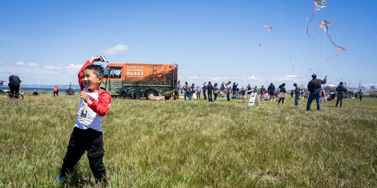 A child smiles flying a kite alongside the Roving Ranger at Crissy Field.