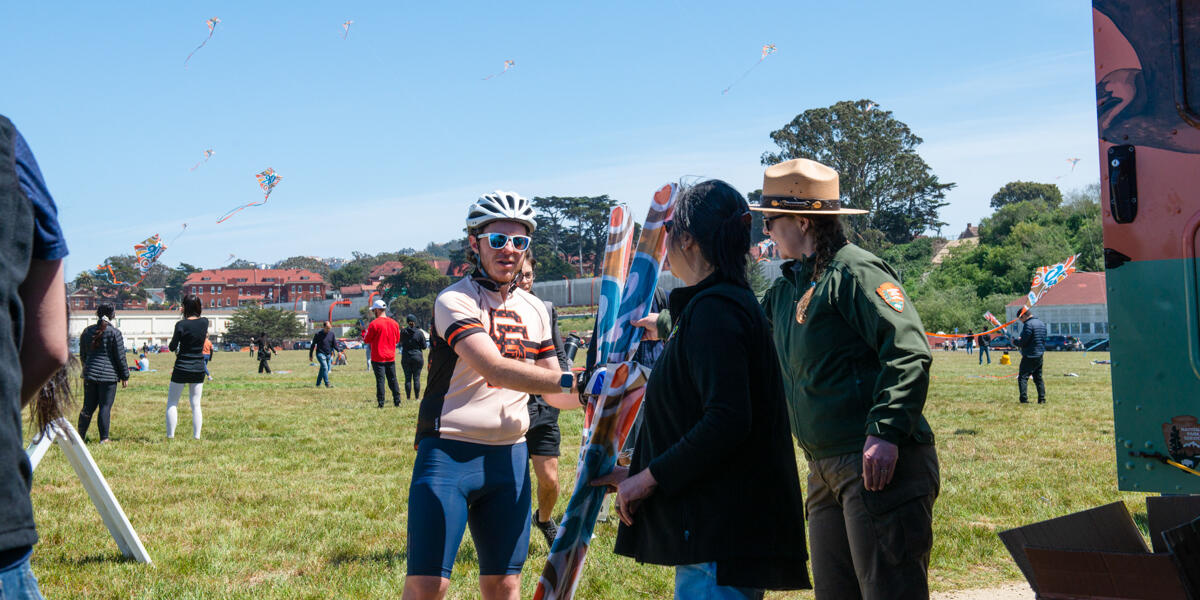 A park visitor receives commemorative Crissy Field 20th anniversary kites from staff at the Roving Ranger.