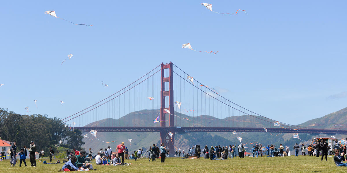A crowd amasses at Crissy Field Kite Day, flying their kites with the Golden Gate Bridge in the background.