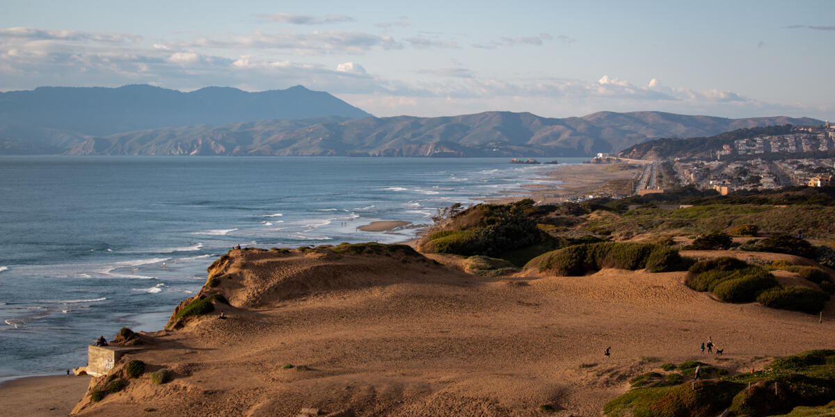 An aerial view of Fort Funston shows the ocean, beach, cliffsides, and looks on to the golden gate.