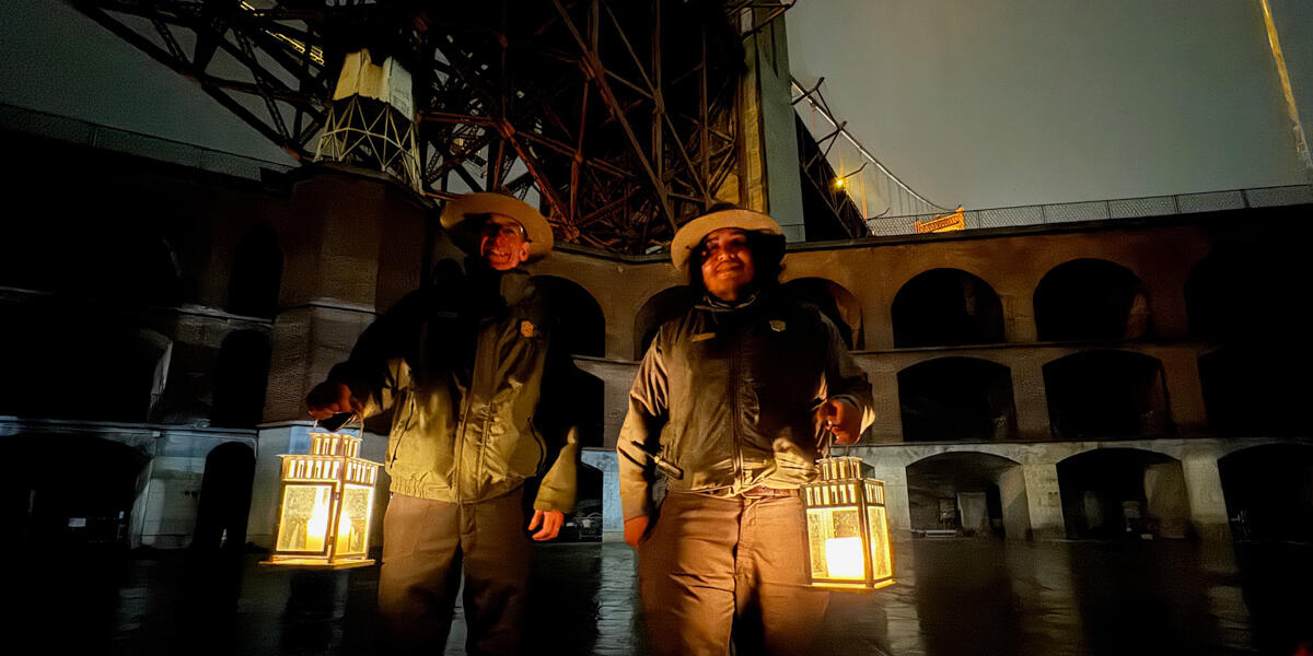 Two NPS National Parks Service rangers holding lanterns at Fort Point for a candlelight tour