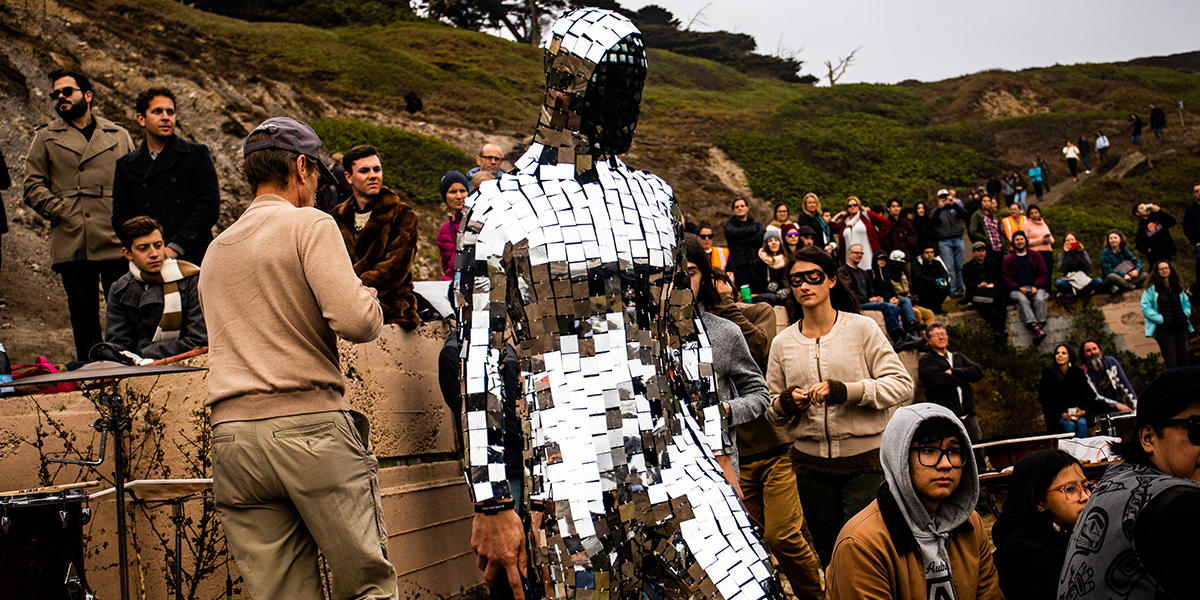 Musician Travis Andrews, dressed like a disco ball, plays the guitar in front of a crowd.