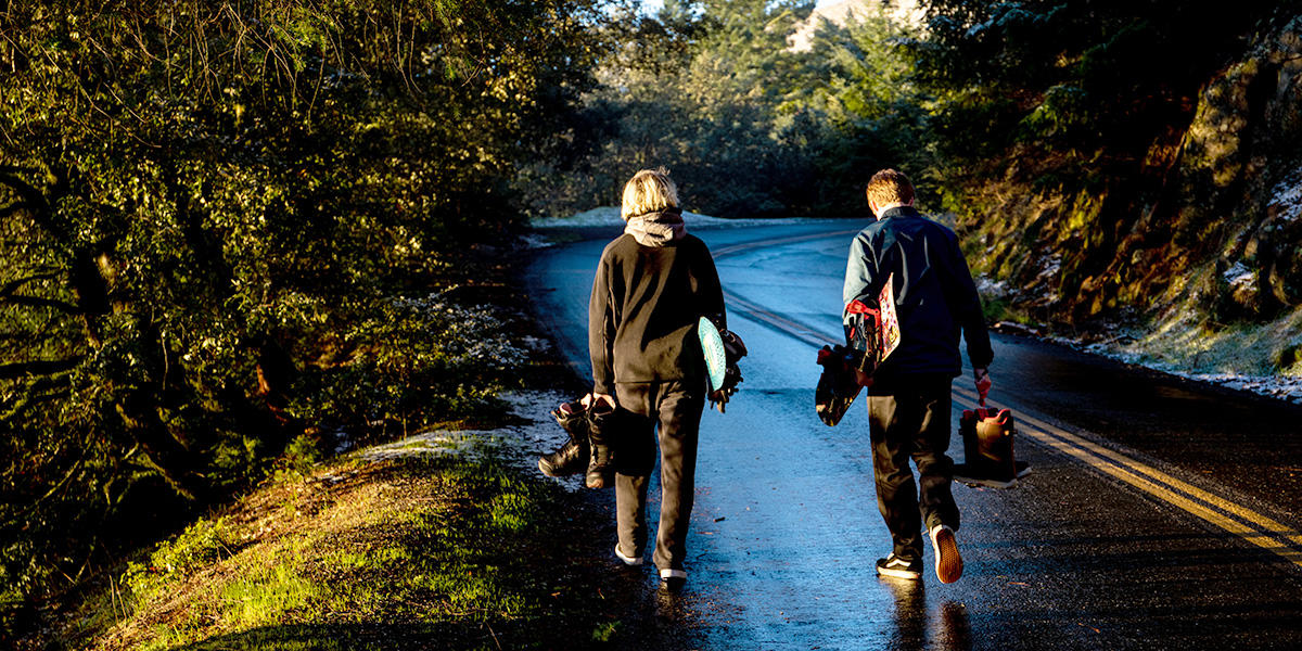 Teens with snowboards walk towards snow.