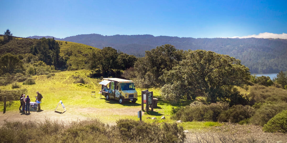 A scenic landscape from Mount Tamalpais. The One Tam Tam Van is parked in the grass with visitors about.