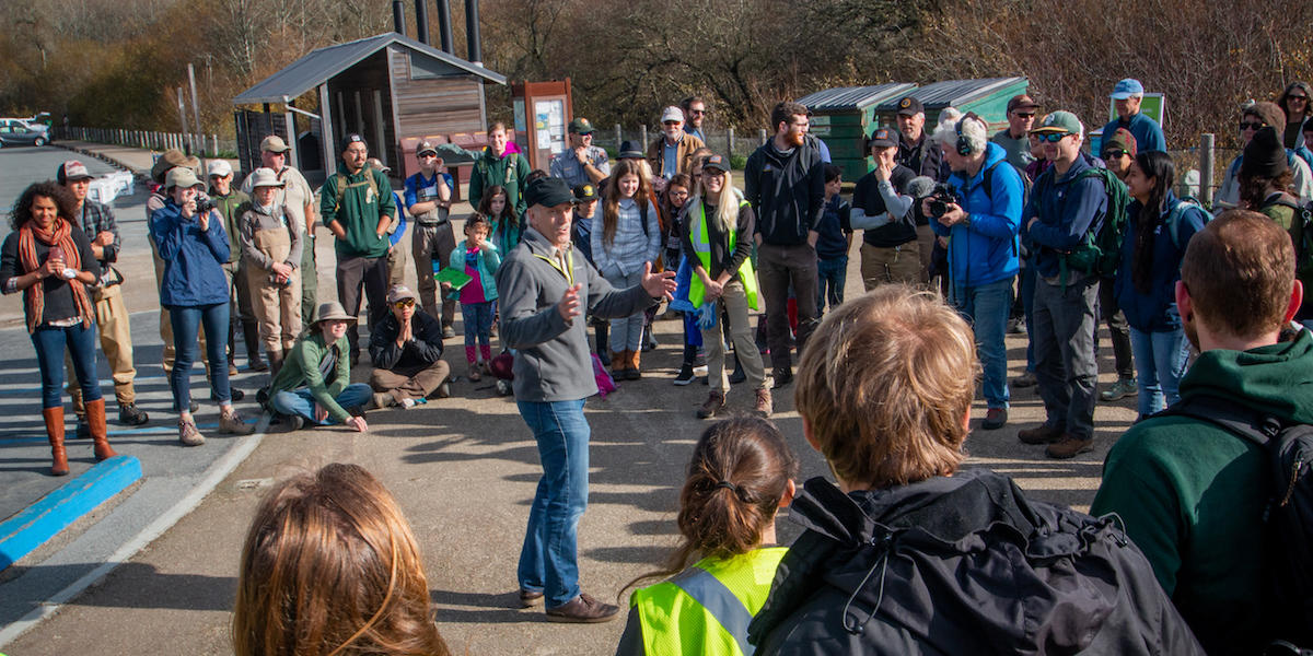 U.S. Fish and Wildlife Service representative gives speech to a encircled crowd at Muir Beach before releasing coho salmon into Redwood Creek. 