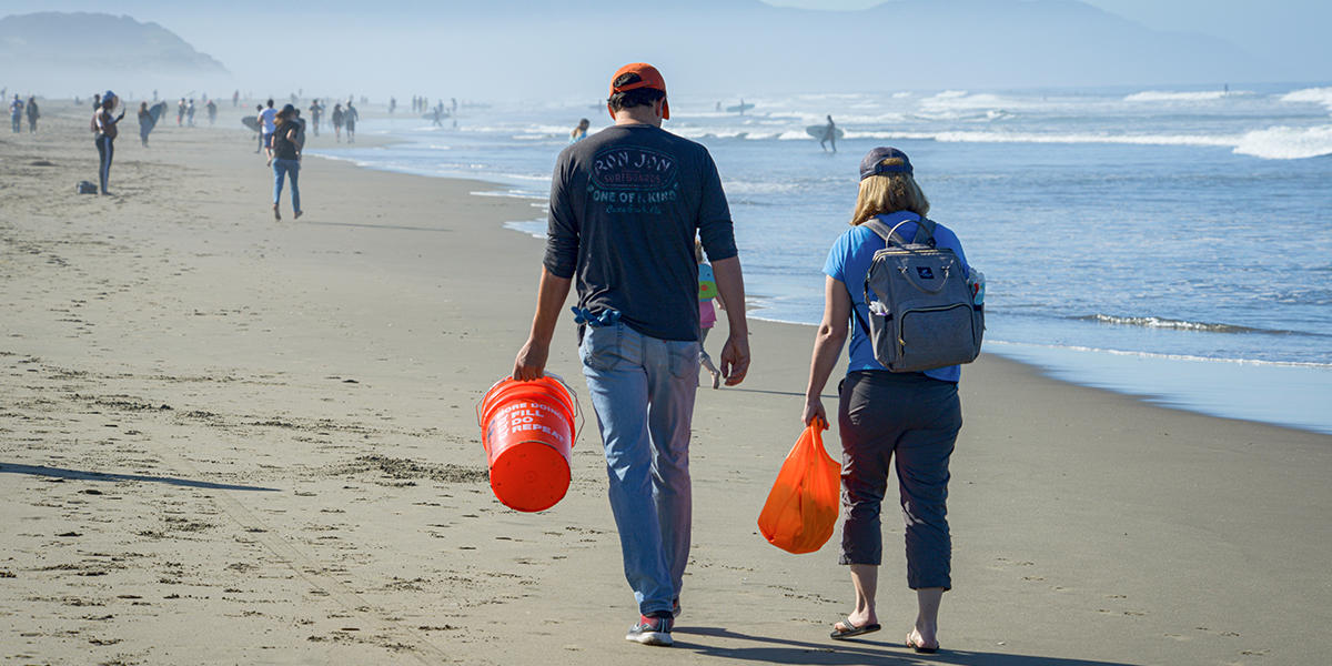 Bare-footed couple wants down Ocean Beach in San Francisco with buckets in hand. 