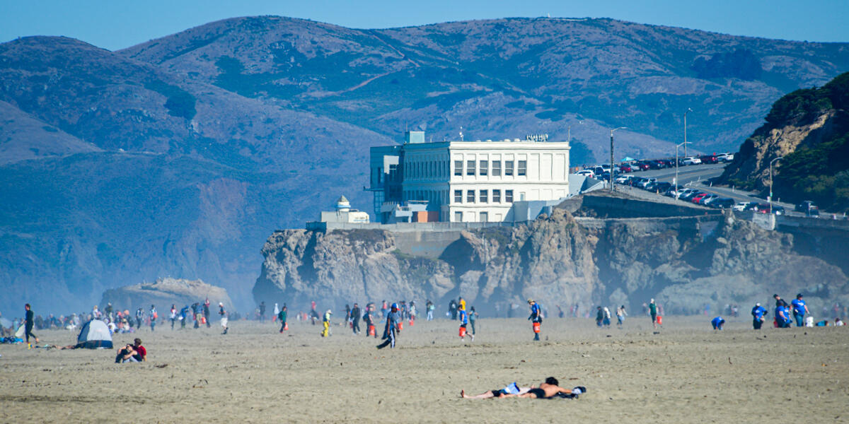 Park visitors and stewardship volunteers for Coastal Cleanup day mingle about on a busy day as the Cliff House restaurant looks over Ocean Beach.