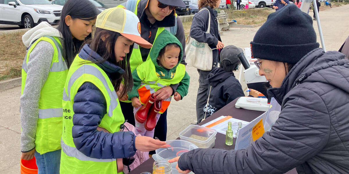A family of beach cleanup volunteers stop by a table to learn about environmentalism