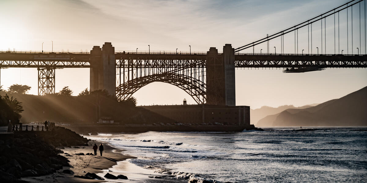 Sunlight filters through the silhouetted Fort Point and Golden Gate Bridge